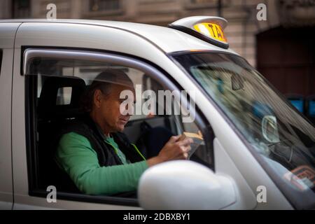 Le chauffeur de taxi Andy Biggs lit un livre dans un taxi noir alors qu'il attend un billet devant la gare Victoria, Londres. Les chauffeurs de taxi londoniens sont confrontés à de longues attentes pour un aller simple après que l'industrie ait connu une forte baisse de la demande, car les restrictions du coronavirus continuent de réduire les déplacements et le travail au bureau. Banque D'Images