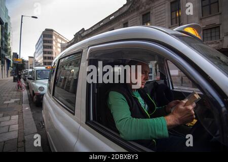 Le chauffeur de taxi Andy Biggs lit un livre dans un taxi noir alors qu'il attend un billet devant la gare Victoria, Londres. Les chauffeurs de taxi londoniens sont confrontés à de longues attentes pour un aller simple après que l'industrie ait connu une forte baisse de la demande, car les restrictions du coronavirus continuent de réduire les déplacements et le travail au bureau. Banque D'Images