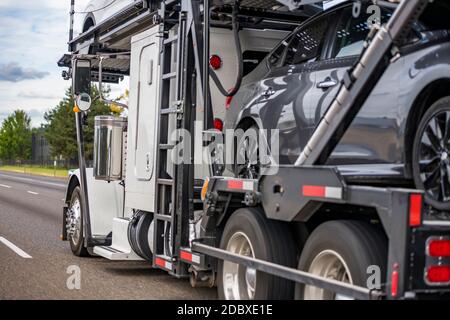 Capot puissant tracteur semi-remorque de transport de voiture blanc Big rig transport de différentes voitures sur une semi-remorque hydraulique réglable à deux niveaux en cours d'exécution sur le Banque D'Images