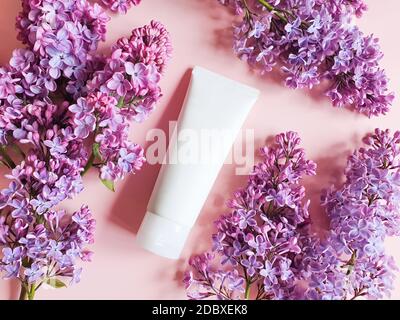 Maquette de tube cosmétique blanc pressé et de fleurs de lilas roses sur fond rose poudreux. Concept de cosmétiques naturels biologiques. Vue de dessus, plat Banque D'Images