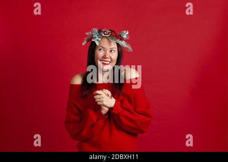 Portrait de joyeux riant jeune femme asiatique en ecstasy class ses mains à la poitrine et regarde loin, sur un fond rouge Banque D'Images