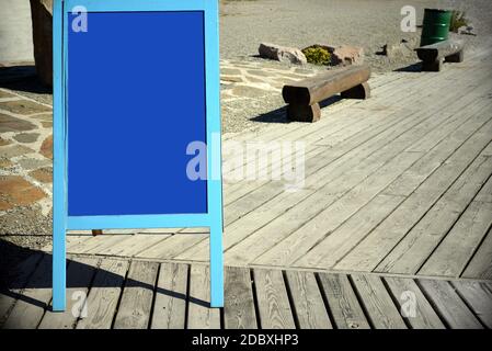 Tableau publicitaire blanc bleu sur la rue de la ville contre chemin en bois avec des bancs près de la caffee. Banque D'Images