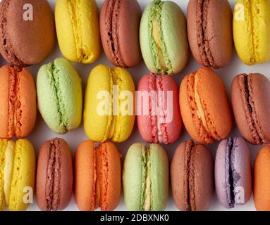 les macarons multicolores cuits ronds se trouvent dans une rangée, plein cadre, gâteau aux amandes brillantes, gros plan Banque D'Images