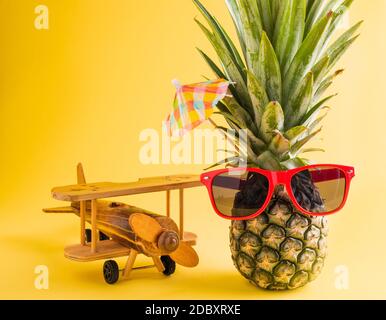 Célébrez le concept de la Journée des ananas d'été, ananas frais drôle dans des supports de lunettes de soleil avec un avion modèle, studio tourné isolé sur fond jaune, Holi Banque D'Images