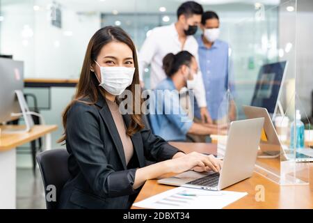 Portrait d'un employé de bureau asiatique femme d'affaires porter un masque de protection travailler dans un nouveau bureau normal avec une équipe interraciale en arrière-plan en tant que social dist Banque D'Images