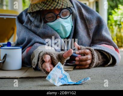 L'homme sans abri saisit son argent après que quelqu'un lui ait laissé l'argent. Il est sans emploi et a faim. Il vit sur la mendicité de la charité des gens. Banque D'Images
