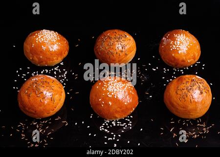 Petits pains blancs croustillants aux graines de sésame. Photo sur fond noir. Des pâtisseries maison sont disposées en rangées. Banque D'Images