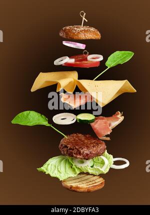 ingrédients de cheeseburger à levants : côtelette de viande juteuse, cheddar, pain de sésame, laitue, rondelles d'oignon blanc, tranche de tomate, concombre sur un b brun Banque D'Images