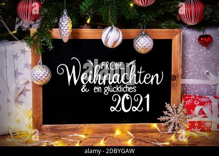 Tableau noir avec calligraphie allemande Frohe Weihnachten und Ein Glueckliches 2021 signifie Joyeux Noël et heureux 2021. Sapin de Noël avec balle, cadeaux A. Banque D'Images
