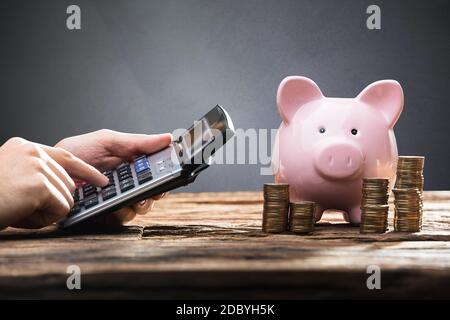 Pile et calculatrice de budget d'argent de Piggybank. Homme travaillant Banque D'Images