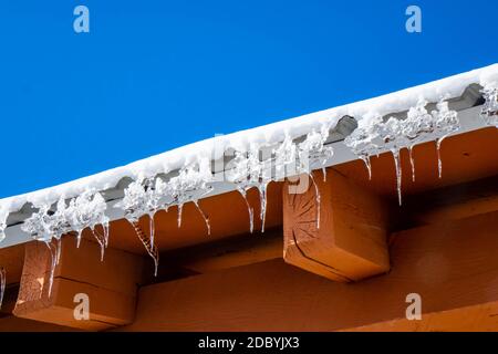 des iclcles suspendus d'un toit avec de la neige fraîche et fondue contre un ciel bleu vif en hiver Banque D'Images