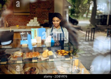 Femme Barista en tablier à la vitrine avec desserts au café. Femme choisissant des bonbons à la cafétéria, serveur au comptoir au bar Banque D'Images