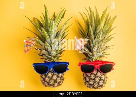 Célébrez le concept de la Journée des ananas d'été, vue du dessus plat de deux ananas drôles en lunettes de soleil, studio tourné isolé sur fond jaune, Holiday su Banque D'Images