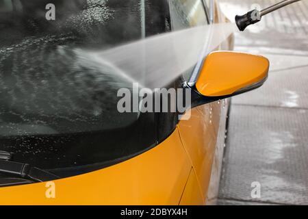 Détails sur jaune foncé vitre avant et arrière de voiture en miroir lavés avec jet d'eau pulvérisée dans carwash. Banque D'Images