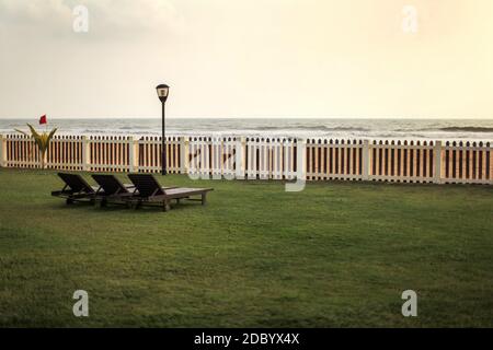 Vue de l'hôtel resort à vide transats sur pelouse verte, la plage et la mer derrière une clôture en bois après le coucher du soleil. Banque D'Images