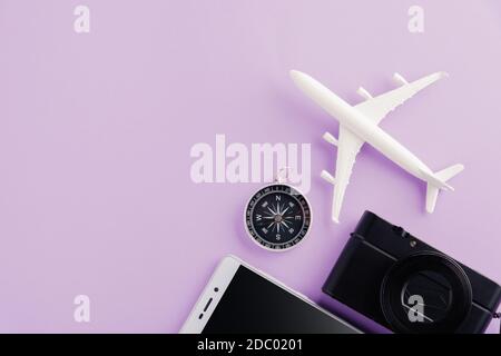 Journée mondiale du tourisme, vue de dessus d'un avion modèle minimal, d'un avion, d'une étoile de mer, d'un réveil, d'une boussole, d'un appareil photo et d'un smartphone, studio tourné en violet Banque D'Images