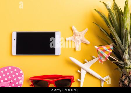 Célébrez le concept de la Journée de l'ananas d'été, plan de dessus avec vue de dessus d'ananas drôle, lunettes de soleil, avion modèle, et écran vide de smartphone, isolé sur jaune Banque D'Images