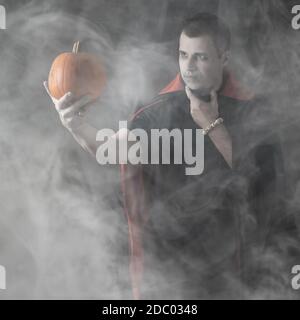 Portrait de vampire masculin d'Halloween. Homme blanc caucasien portant une citrouille d'orange habillé et stylisé pour un nosferatu sur fond sombre fumé ou brumeux Banque D'Images