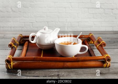 Petite théière et tasse en céramique blanche de la vapeur chaude thé noir avec cuillère en argent servi sur de vieux bac en bambou placé sur bois gris 24. Banque D'Images