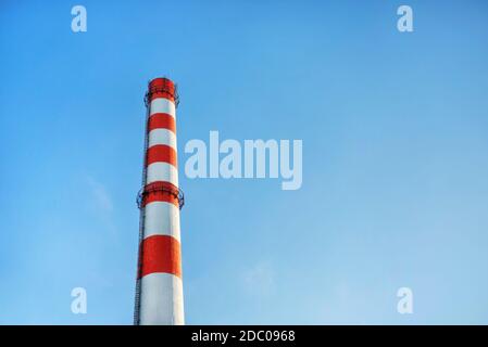 Cheminée d'usine avec bandes rouges et blanches sur fond bleu ciel. Banque D'Images