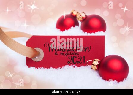 Étiquette rouge avec la calligraphie allemande Frohe Weihnachten und Ein Glueckliches 2021 signifie Joyeux Noël et UN heureux 2021. Décoration boule de Noël. Bo brillant Banque D'Images