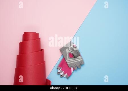 gants de sport et tapis en néoprène rouge torsadé pour le sport de yoga sur fond bleu rose, vue du dessus Banque D'Images