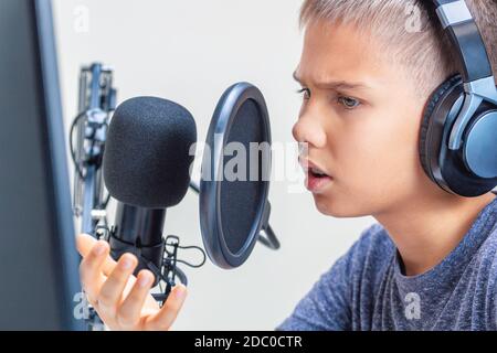 Adolescent portant un casque qui regarde l'écran de l'ordinateur et parle utilisation du jeu de microphones Banque D'Images