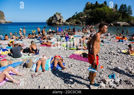 Sicile, Italie. Les touristes se rassemblent sur la plage de Spiaggia Isola Bella lors d'une chaude journée ensoleillée. Banque D'Images