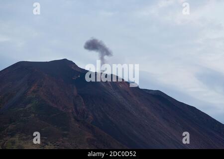 Sicile, Italie. Un panache sombre de fumée volcanique et de cendres s'élève du volcan actif de Stromboli. Banque D'Images