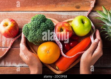 Journée mondiale de la nourriture, vue de dessus de divers fruits et légumes frais biologiques dans la plaque de coeur et la femme utilisation mains tenir la plaque, prise en studio sur table en bois, Banque D'Images