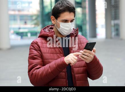 Homme portant un masque chirurgical à l'aide d'une application pour smartphone dans une ville moderne Banque D'Images