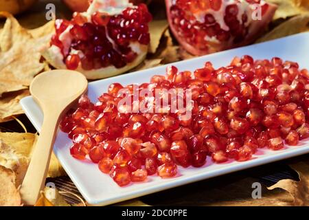 gros plan des graines rouges du fruit de grenade préparé sur une assiette prête à manger avec une cuillère en bois. fond de feuilles d'arbres sèches tombées dans l'autum Banque D'Images