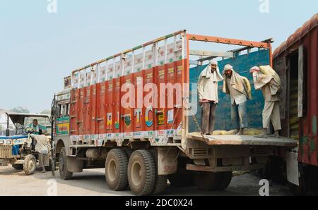 Les travailleurs manuels déplacent de lourds sacs de ciment du train chargé au camion d'attente dans des conditions chaudes et poussiéreuses à Mathura, Uttar Pradesh, Inde. Banque D'Images