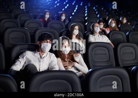 Foyer sélectif de l'homme et de la femme qui apprécie le film pendant la pandémie mondiale, regardant l'écran. Jeunes caucasiens regardant un film au cinéma, portant des masques blancs. Concept de distanciation sociale. Banque D'Images