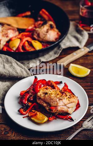 Cuisses de poulet cuites au four avec poivrons rouges et citron sur une assiette blanche. Banque D'Images