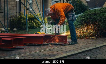 Workman portant des vêtements de protection coupant à travers l'acier RSJ avec une scie circulaire de métal créant des étincelles sur un site de construction domestique, en Angleterre Banque D'Images