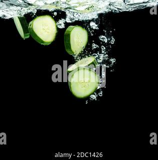 Tranches de bio concombre éclaboussant de l'eau isolée sur fond noir. Concept de cosmétiques hydratants pour la peau Banque D'Images