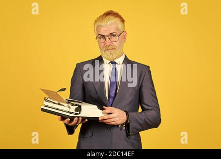 Magasin de marchandises d'occasion. Objets anciens du vendeur. Connaisseur des valeurs vintage. Machine à écrire vintage. Les hommes d'affaires utilisent la technologie rétro. Homme mûr teint les cheveux de barbe fond jaune. Les vieux habitudes de l'auteur de bâton. Banque D'Images
