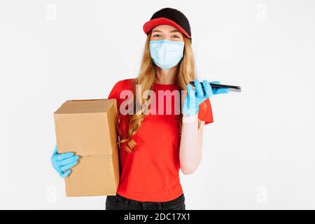 Un messager en uniforme, portant des gants médicaux en caoutchouc et un masque médical, tient des boîtes en carton et utilise un téléphone portable sur fond blanc. bts en ligne Banque D'Images