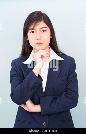 Une jeune fille adolescente portant un costume avec main sur le menton isolée sur fond bleu Banque D'Images