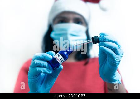 vaccin covid-19 concept de noël. femme médecin avec masque facial dans l'ensemble du père noël tenant le vaccin covid à l'intérieur d'un flacon bleu et d'une seringue Banque D'Images