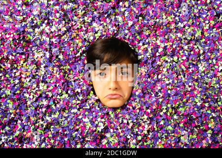 Jeune garçon triste visage étant entouré de confetti de couleur Banque D'Images