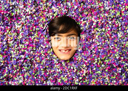 Jeune garçon visage souriant entouré de confettis colorés Banque D'Images