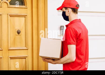 Un coursier dans un masque médical de protection avec des boîtes dans ses mains livre des colis. Prestation de services en termes de quarantaine, coronavirus pandémique Banque D'Images