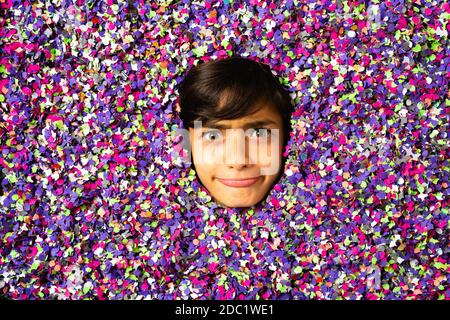 Jeune garçon visage faisant des grimaces et étant entouré de couleur confettis Banque D'Images