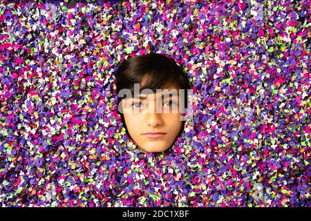 Le visage du jeune garçon est entouré de confettis colorés Banque D'Images