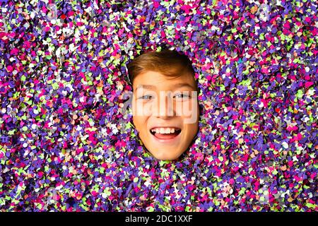 Visage souriant de jeune garçon entouré de confettis colorés Banque D'Images