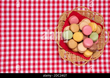 Pâtisseries, desserts et bonbons. Vue de dessus des biscuits de macaron français d'origine multicorde sont disposés dans un panier sur une serviette à carreaux rouges. Concept fête, anniversaire et invitation. Copier l'espace. Banque D'Images