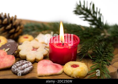 Bougie rouge allumée entre les biscuits de Noël décorés sur un panneau en bois devant un fond blanc Banque D'Images