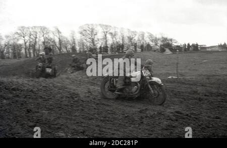 À la fin des années 1950, des concurrents masculins prennent part à un événement de brouille de motocyclettes, traversant une pente boueuse. Inventée en 1924, à Camberley, Surrey, Angleterre, les motos utilisées pour se bousculer dans les années 50 et au début des années 60 étaient peu différentes des motos de route de l'époque, avec très peu de suspension. Aujourd'hui, ce sport est connu sous le nom de motocross, le nom français de motocyclisme de fond, et appelé Supercross aux États-Unis. Banque D'Images